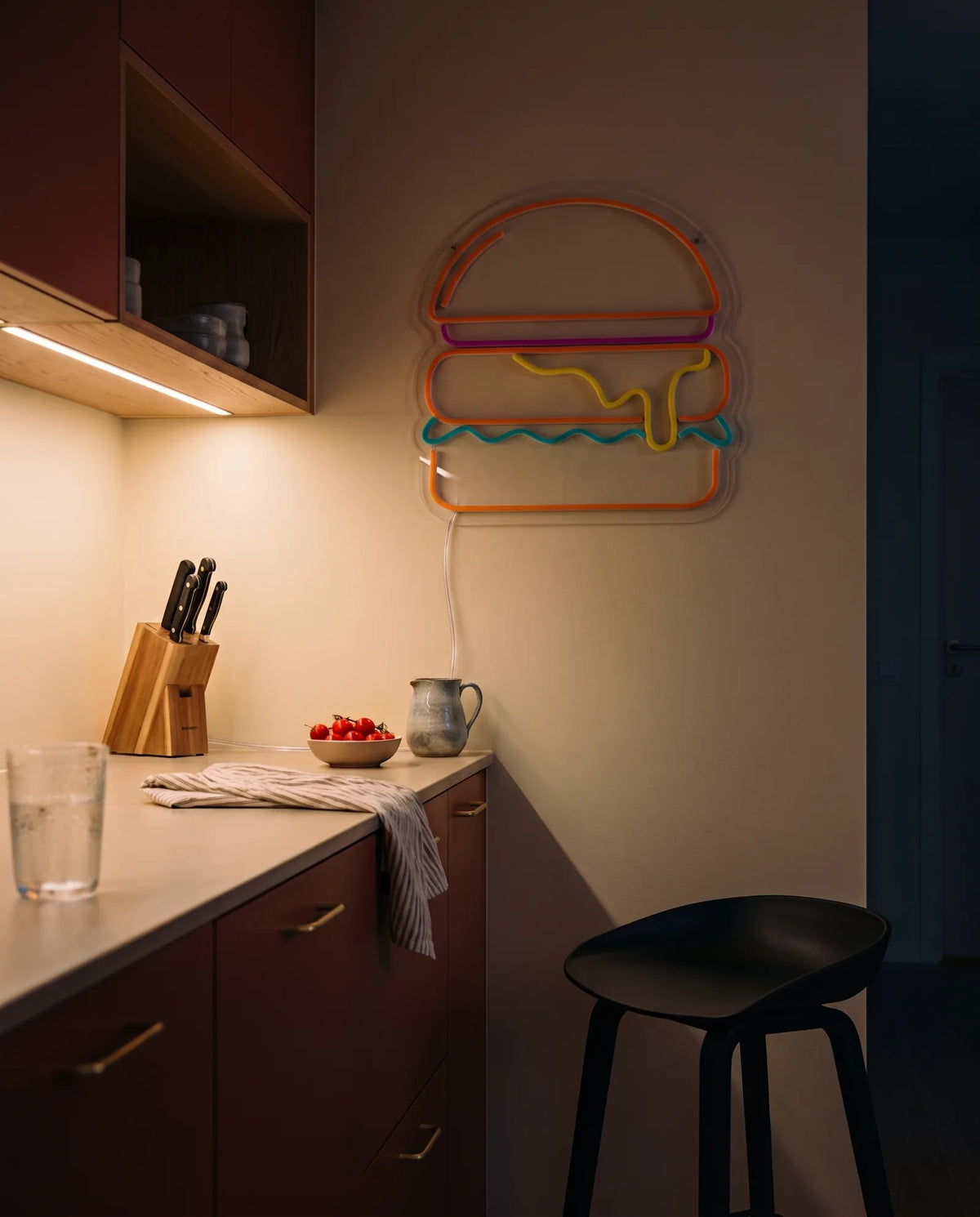 Néon burger éteint dans une cuisine claire le soir, tabouret noir et plan de travail rangé