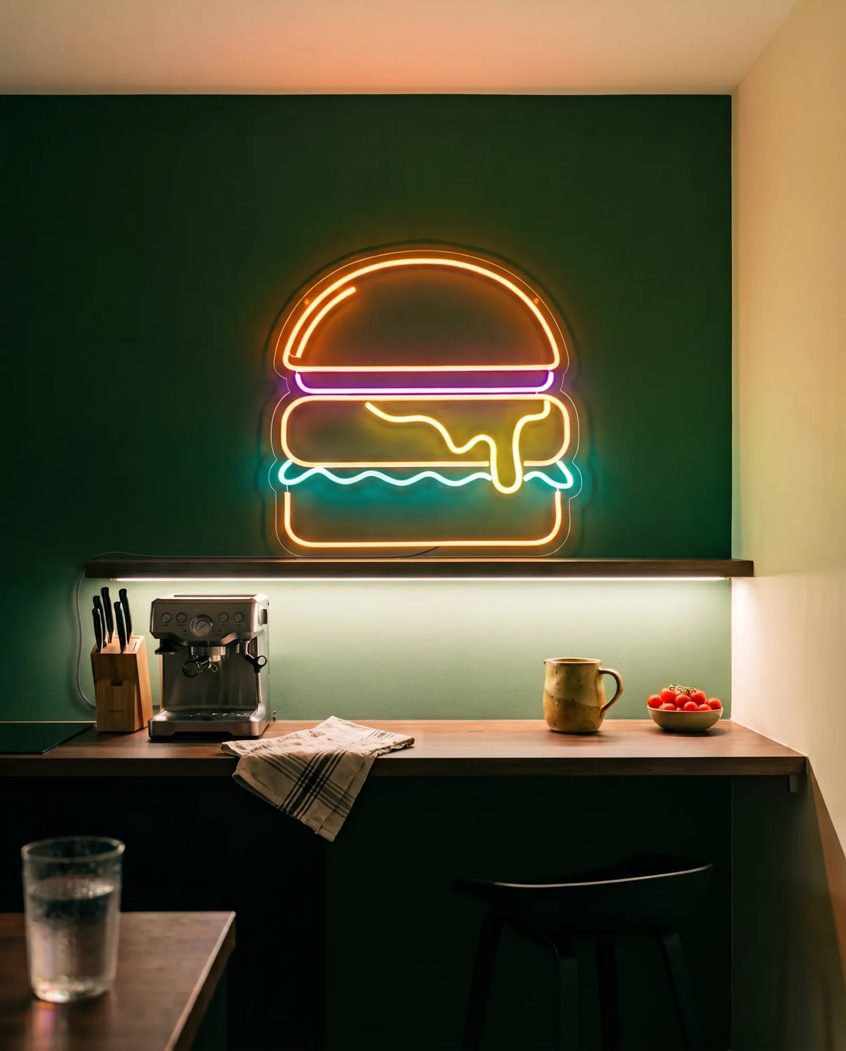 Néon LED burger sur un mur vert sapin au-dessus d’une étagère, machine à espresso et cruche en grès