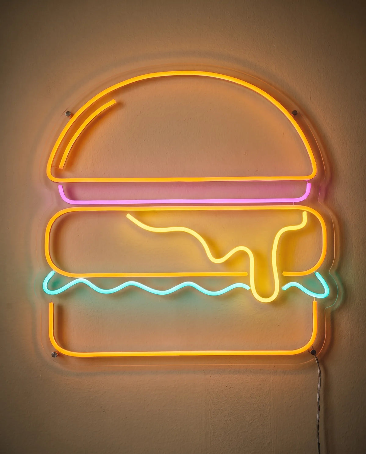 Néon burger fondant de face sur mur peint, fromage jaune qui coule et salade ondulée