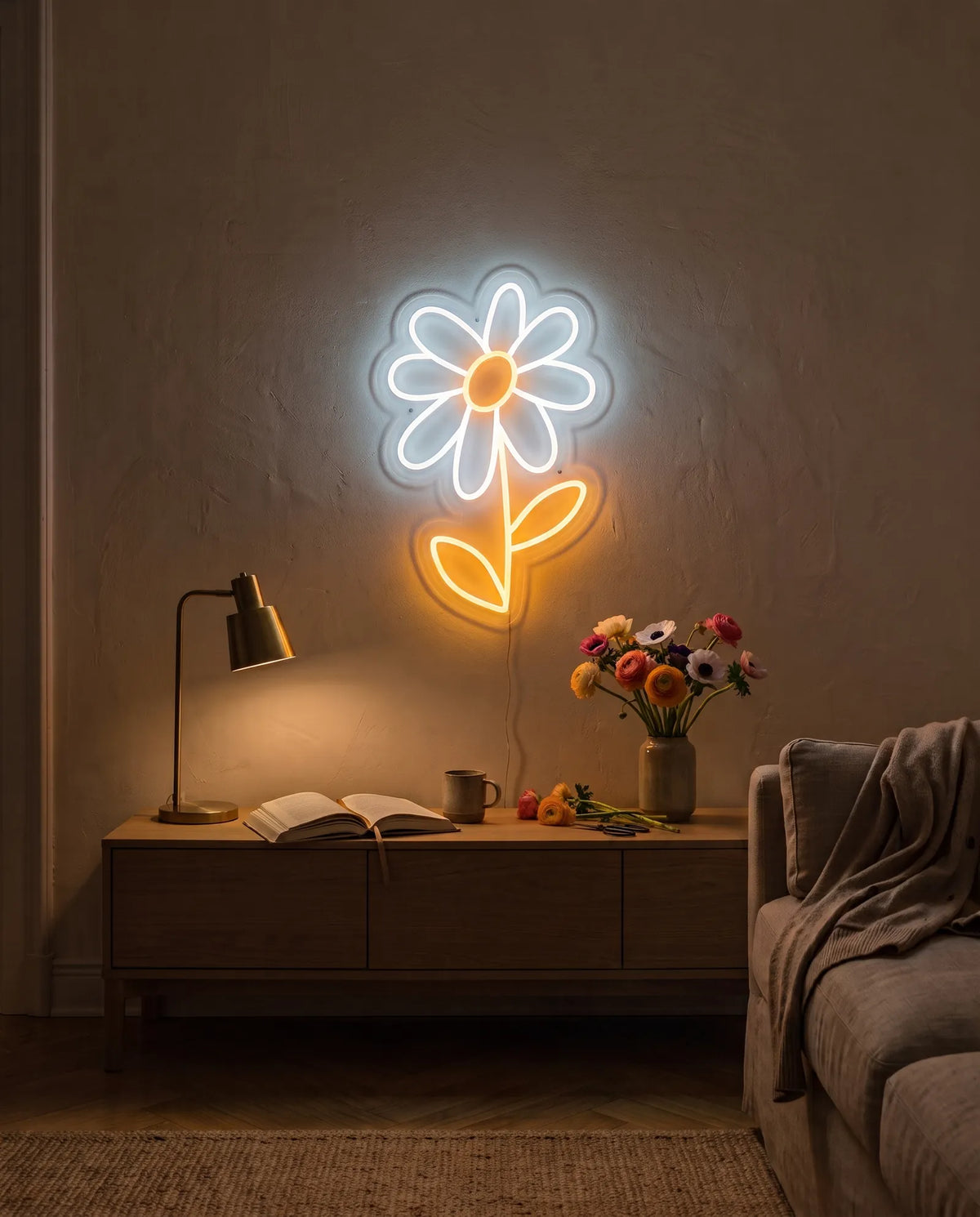 Néon fleur marguerite blanc et doré allumé au-dessus d’une console en bois, bouquet de renoncules et livre ouvert