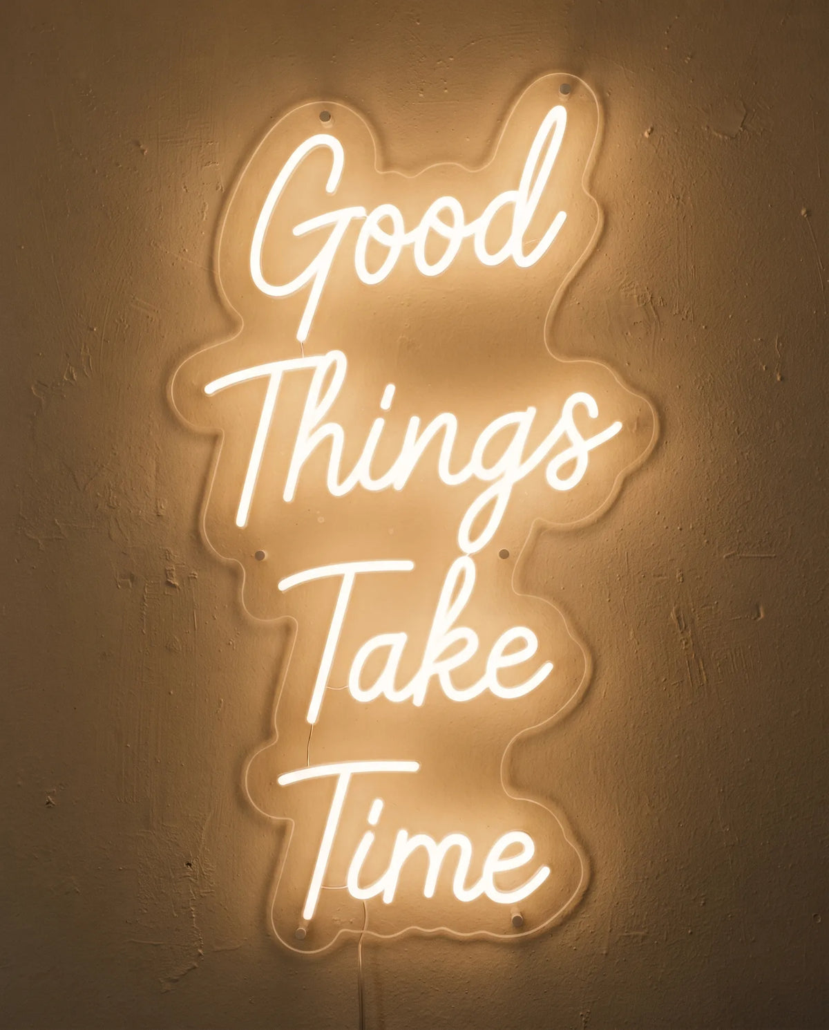 Néon Good Things Take Time de face sur mur peint, quatre mots manuscrits sur quatre lignes
