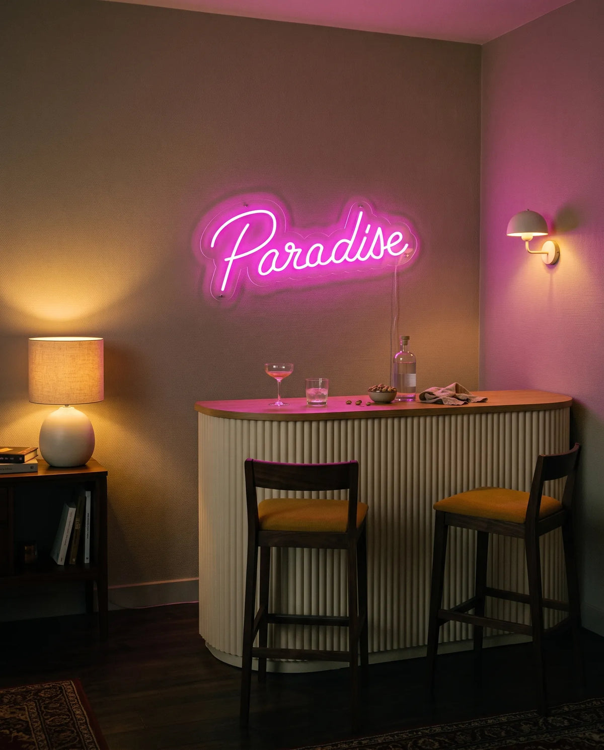 Néon paradise rose allumé au-dessus d’un meuble bar cannelé, coupe à cocktail, tabourets et applique