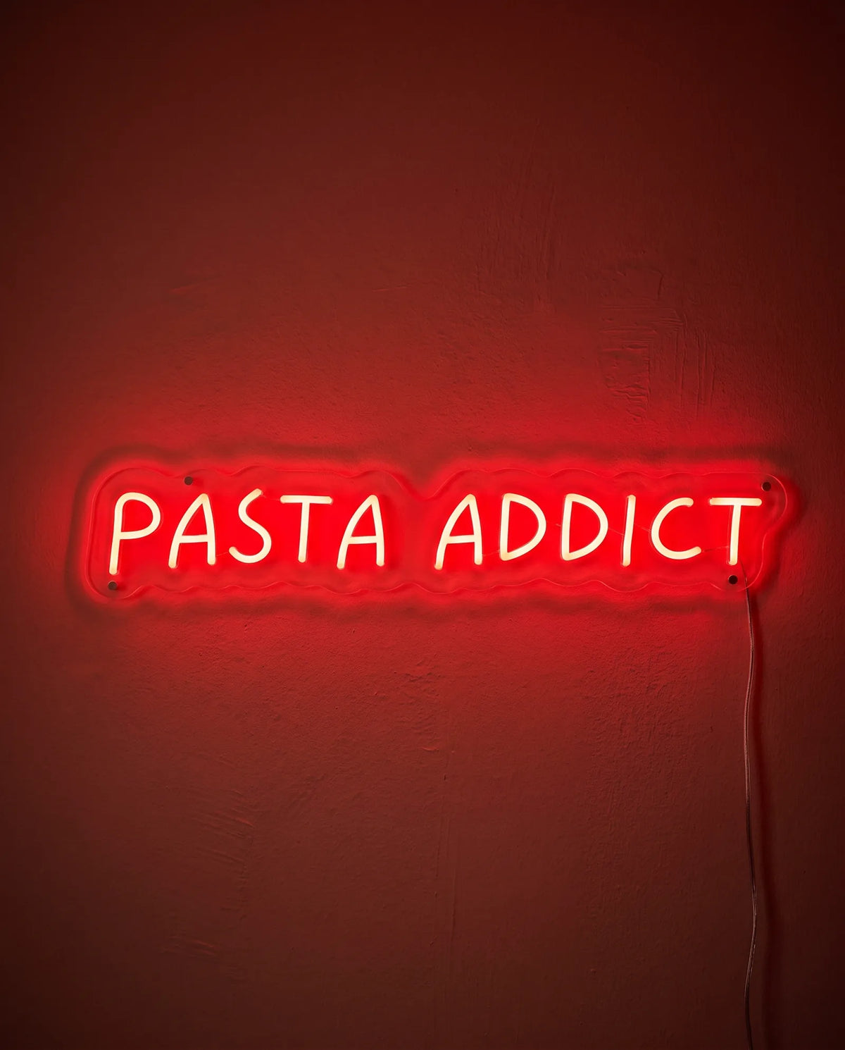 Néon Pasta Addict de face sur mur peint, capitales manuscrites rouges