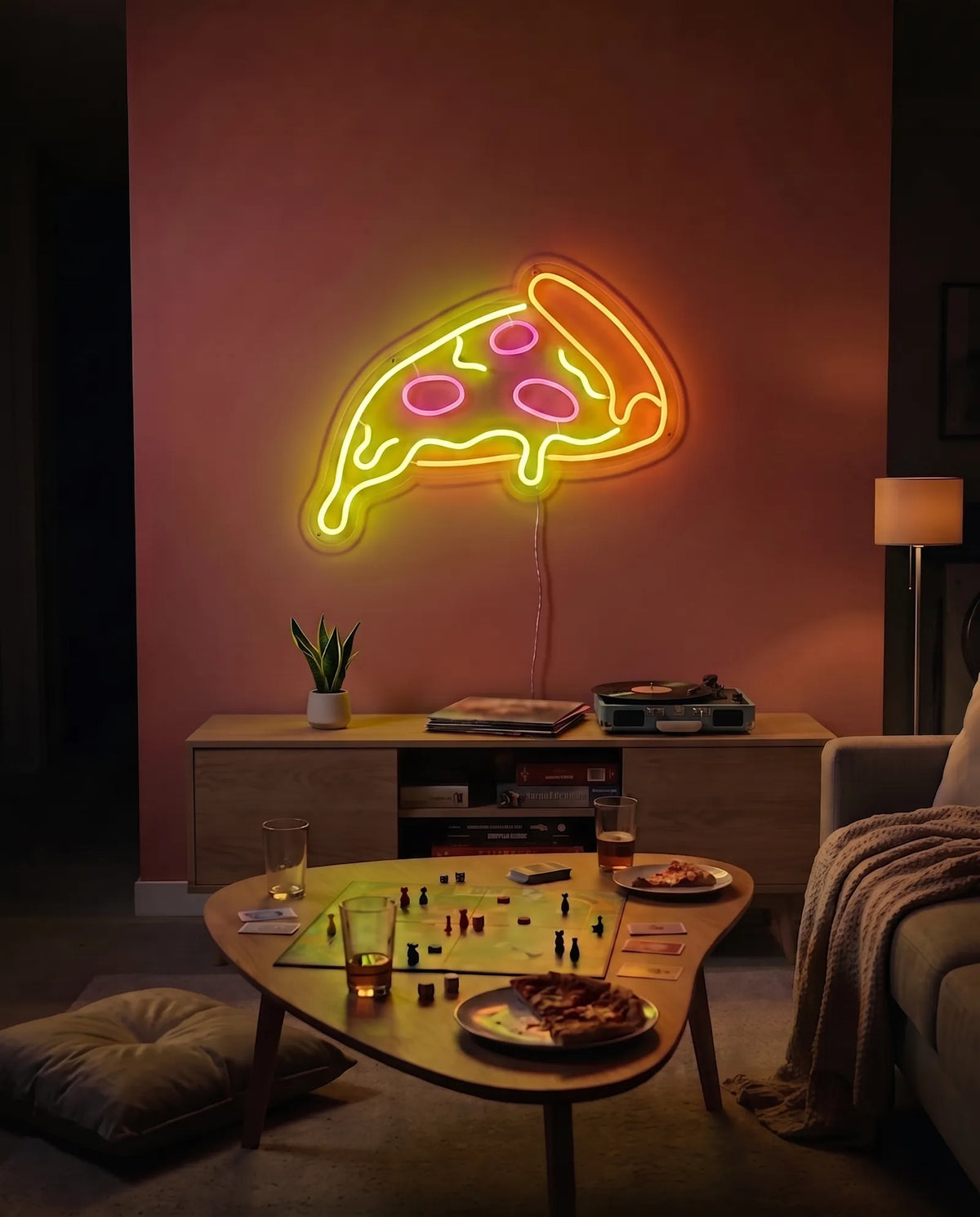 Néon pizza orange, jaune et rouge allumé dans un salon, table basse avec jeu de société et parts de pizza