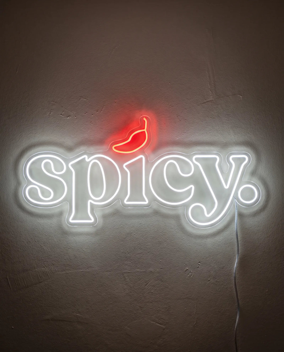 Néon spicy de face sur mur peint, lettres blanc froid surmontées d’un piment rouge