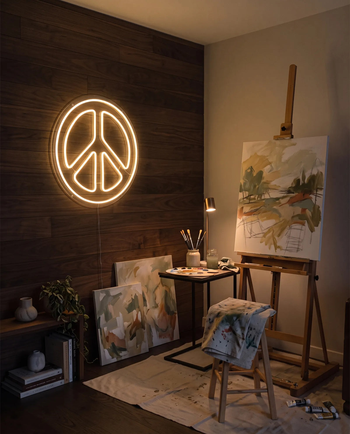 Néon peace and love blanc chaud allumé sur un mur en bois sombre, chevalet, toiles et palette de peinture
