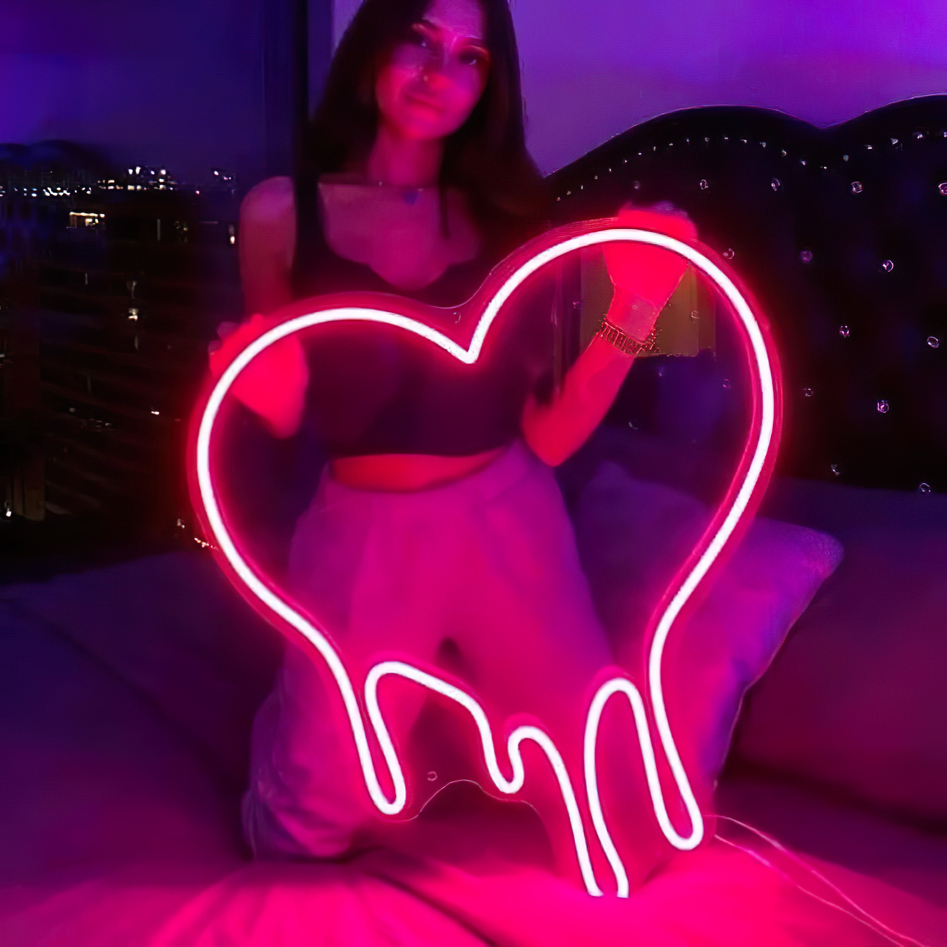 Une femme tient un néon cœur fondu dans une chambre 