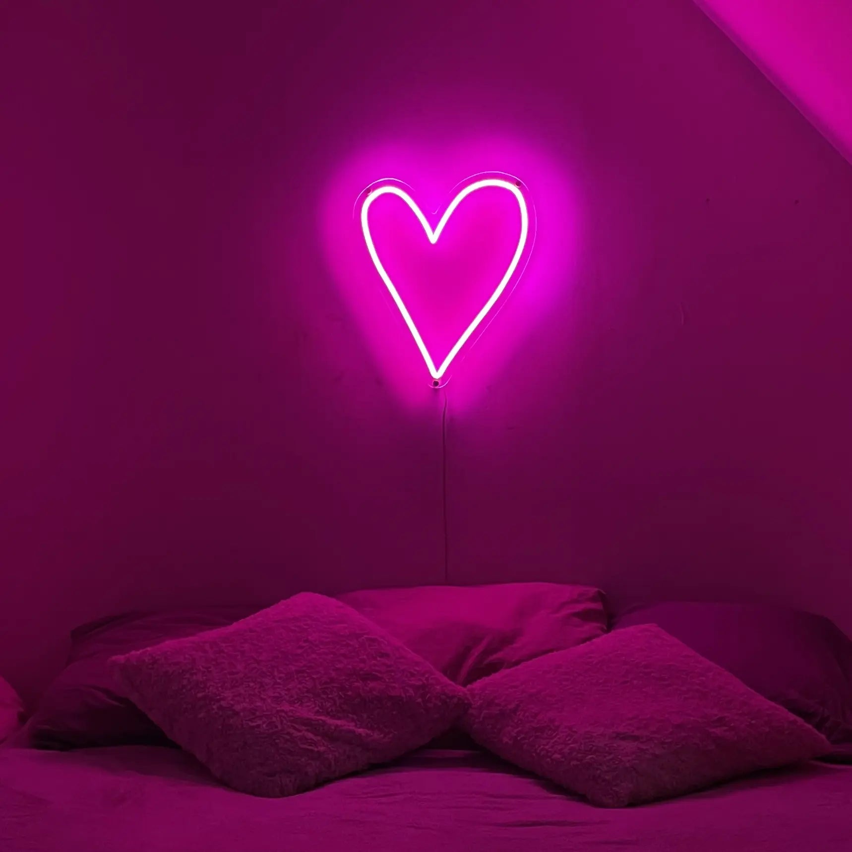 Néon cœur rose dans une chambre au dessus d'un lit 