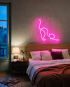 Néon chat rose au-dessus d’une tête de lit en bois, chambre à l’heure bleue et lampe de chevet allumée
