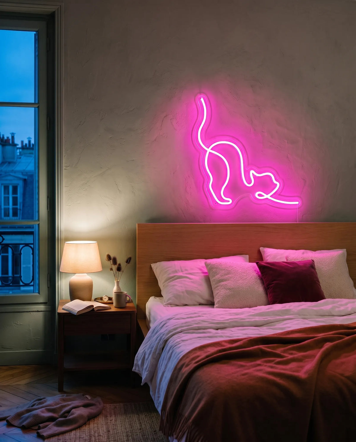 Néon chat rose au-dessus d’une tête de lit en bois, chambre à l’heure bleue et lampe de chevet allumée