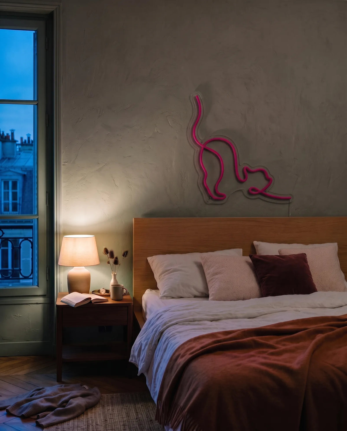 Néon chat rose éteint au-dessus d’une tête de lit en bois, chambre à l’heure bleue et lampe de chevet allumée