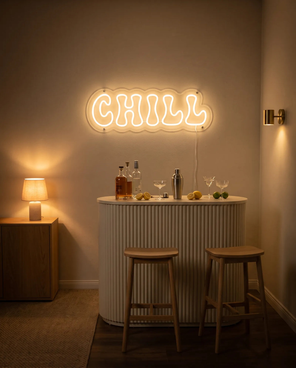 Néon LED chill au-dessus d’un meuble bar cannelé, shaker, citrons, verres à cocktail et tabourets en bois