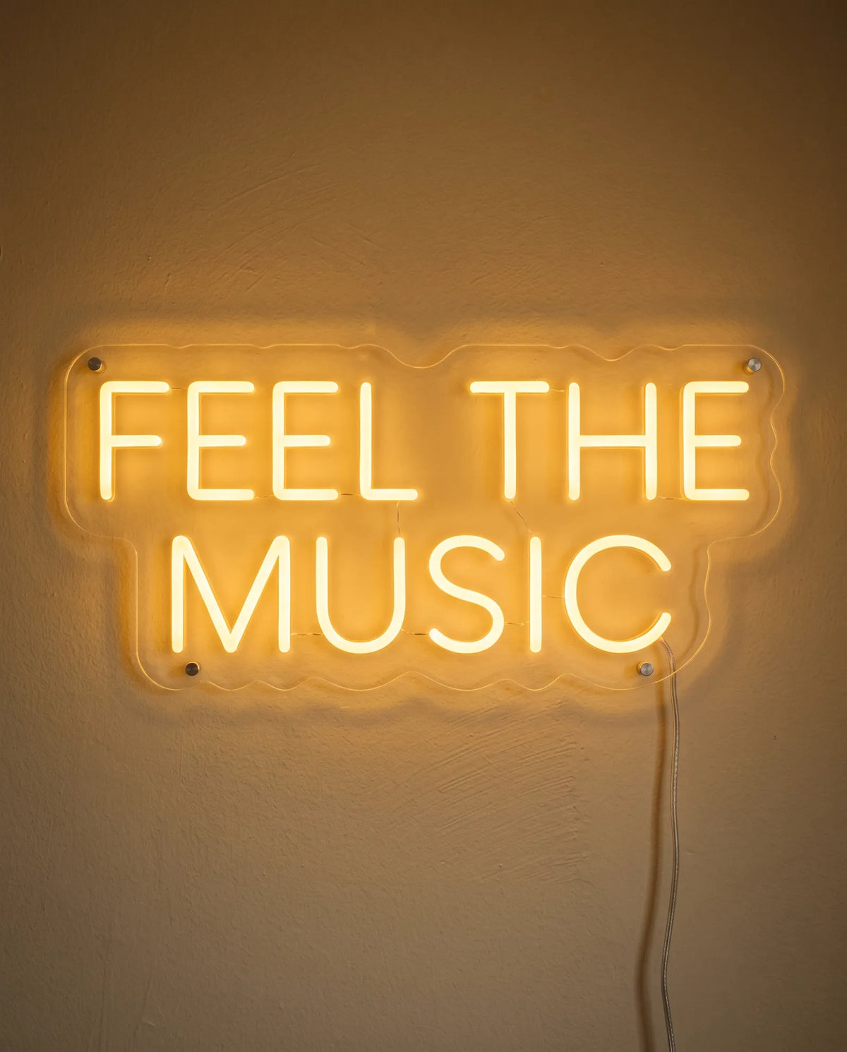 Néon Feel The Music de face sur mur peint, lettres capitales dorées sur deux lignes