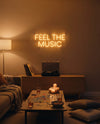 Néon Feel The Music doré allumé au-dessus d’une platine vinyle, table basse avec jeu de société et bougies