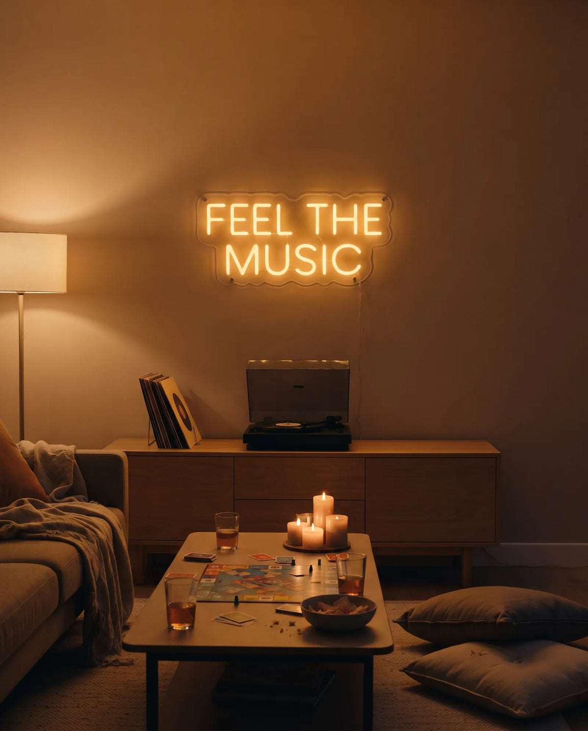 Néon Feel The Music doré allumé au-dessus d’une platine vinyle, table basse avec jeu de société et bougies