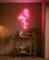 Néon LED flamant rose allumé au-dessus d’une desserte de bar en laiton, coupes et bouteilles sur mur terracotta