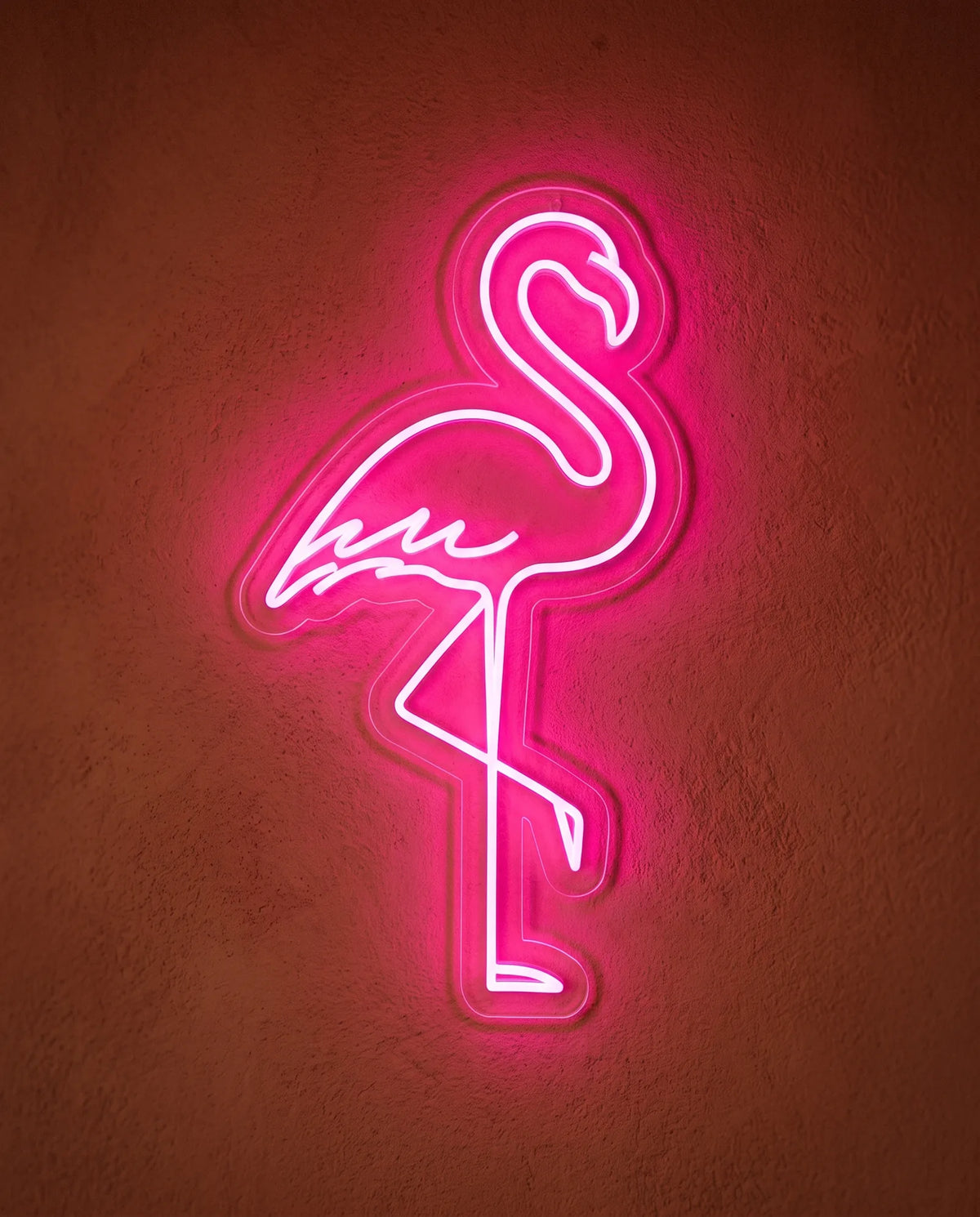 Néon flamant rose de face sur mur terracotta, silhouette posée sur une patte en lumière rose