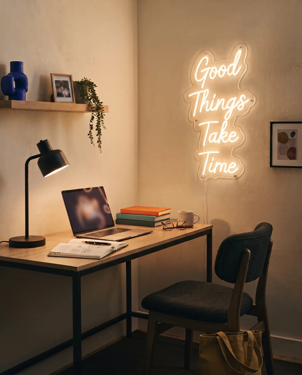 Néon LED citation Good Things Take Time près d’un bureau, ordinateur, carnet de notes et lampe noire