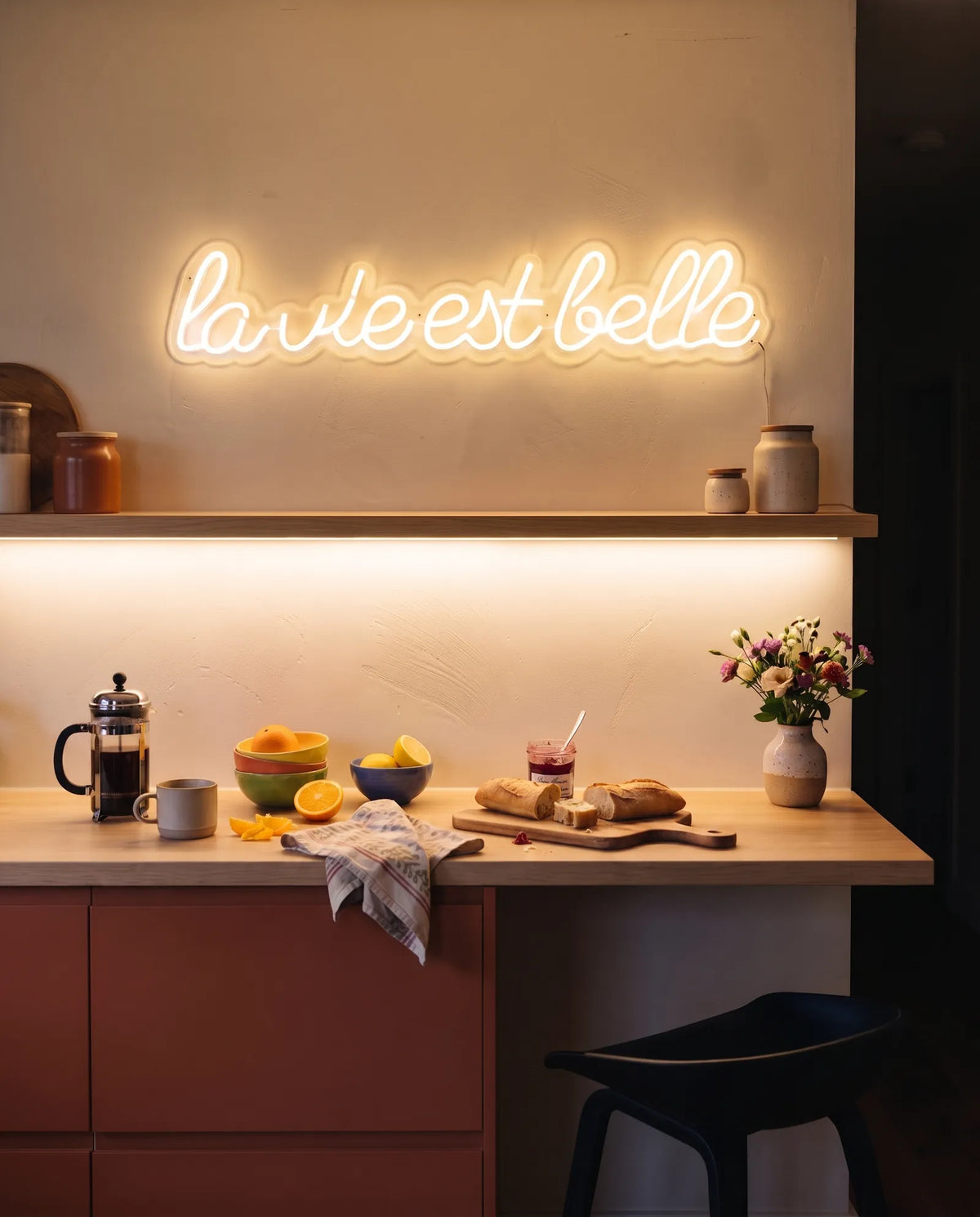 Néon la vie est belle blanc chaud allumé au-dessus d’une étagère de cuisine, baguette, oranges et cafetière