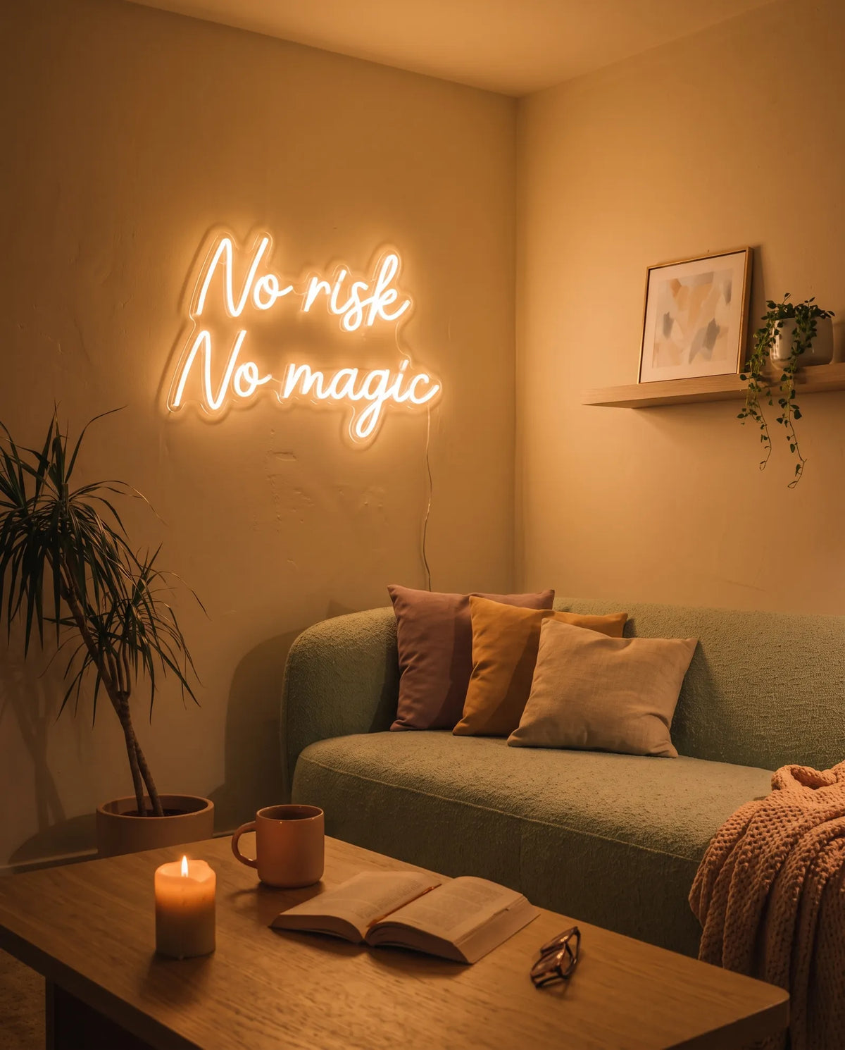 Néon No Risk No Magic blanc chaud allumé au-dessus d’un canapé vert, bougie et livre ouvert sur la table basse