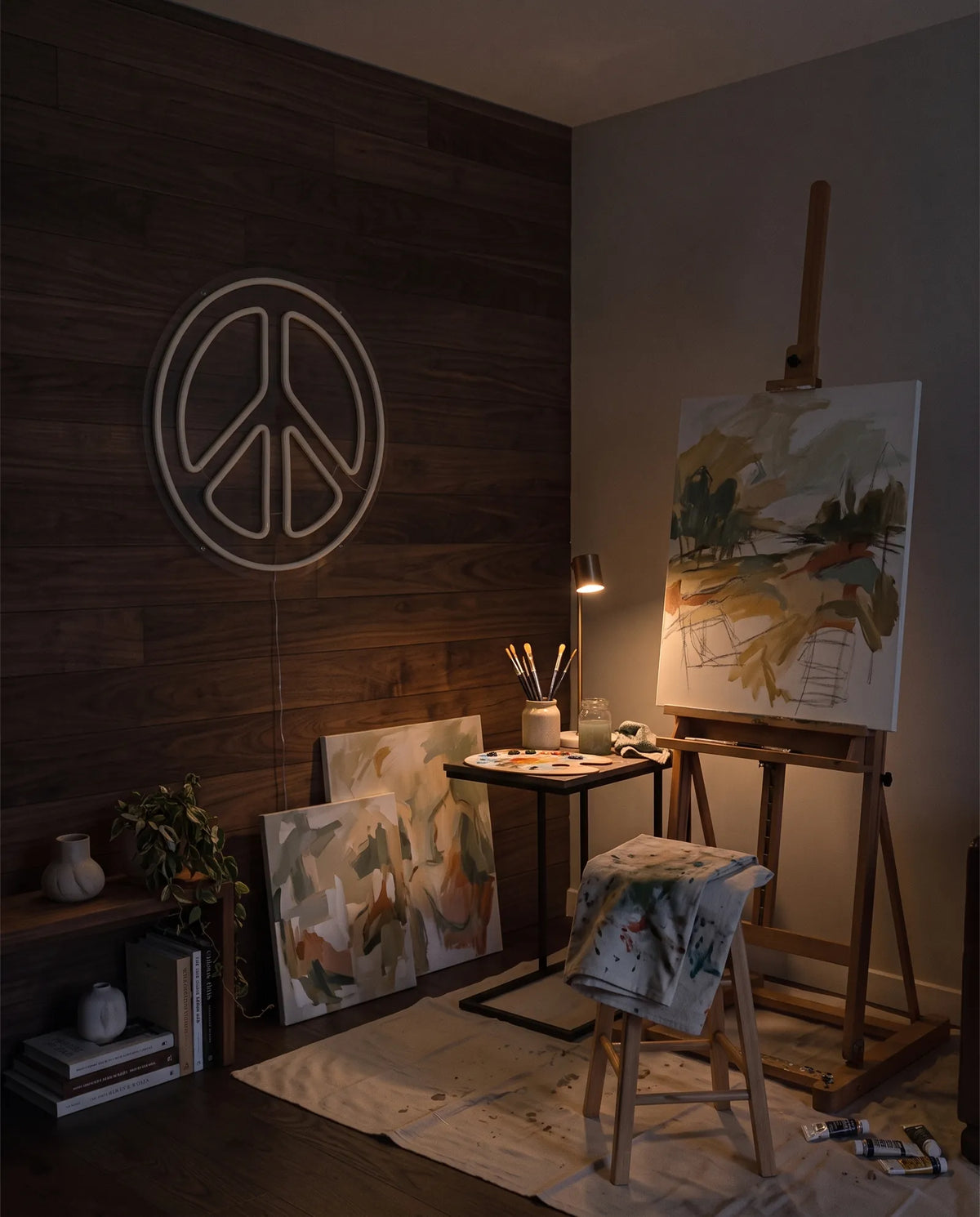 Néon peace and love éteint dans un atelier de peinture le soir, chevalet, tabouret et toiles au sol