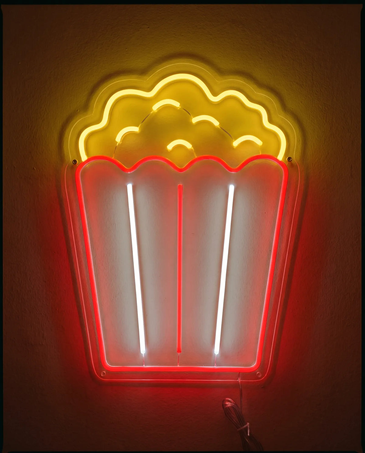 Néon popcorn de face sur mur peint, pot rayé rouge et blanc froid, maïs jaune qui déborde