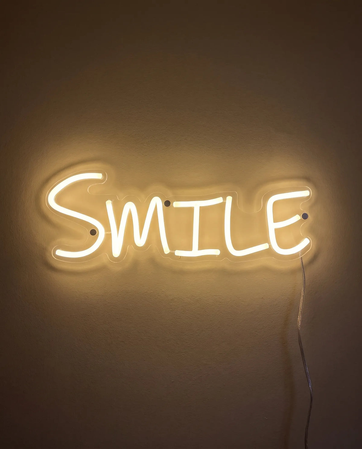 Néon smile de face sur mur peint, lettres manuscrites blanc chaud