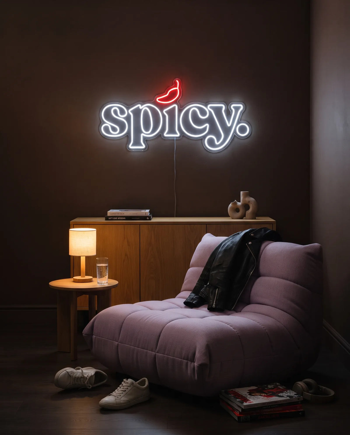 Néon spicy blanc froid et rouge allumé au-dessus d’un buffet en bois, fauteuil gris, blouson en cuir et lampe