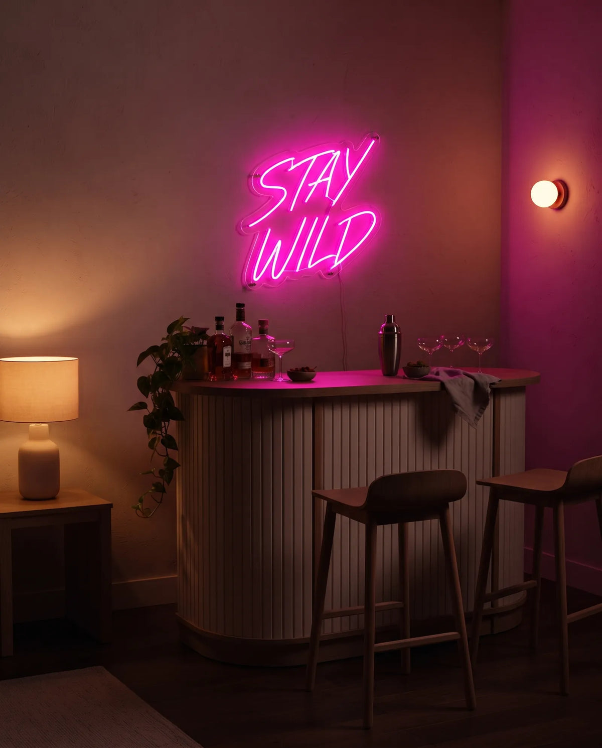 Néon LED citation Stay Wild au-dessus d’un meuble bar cannelé, shaker, coupes et tabourets en bois
