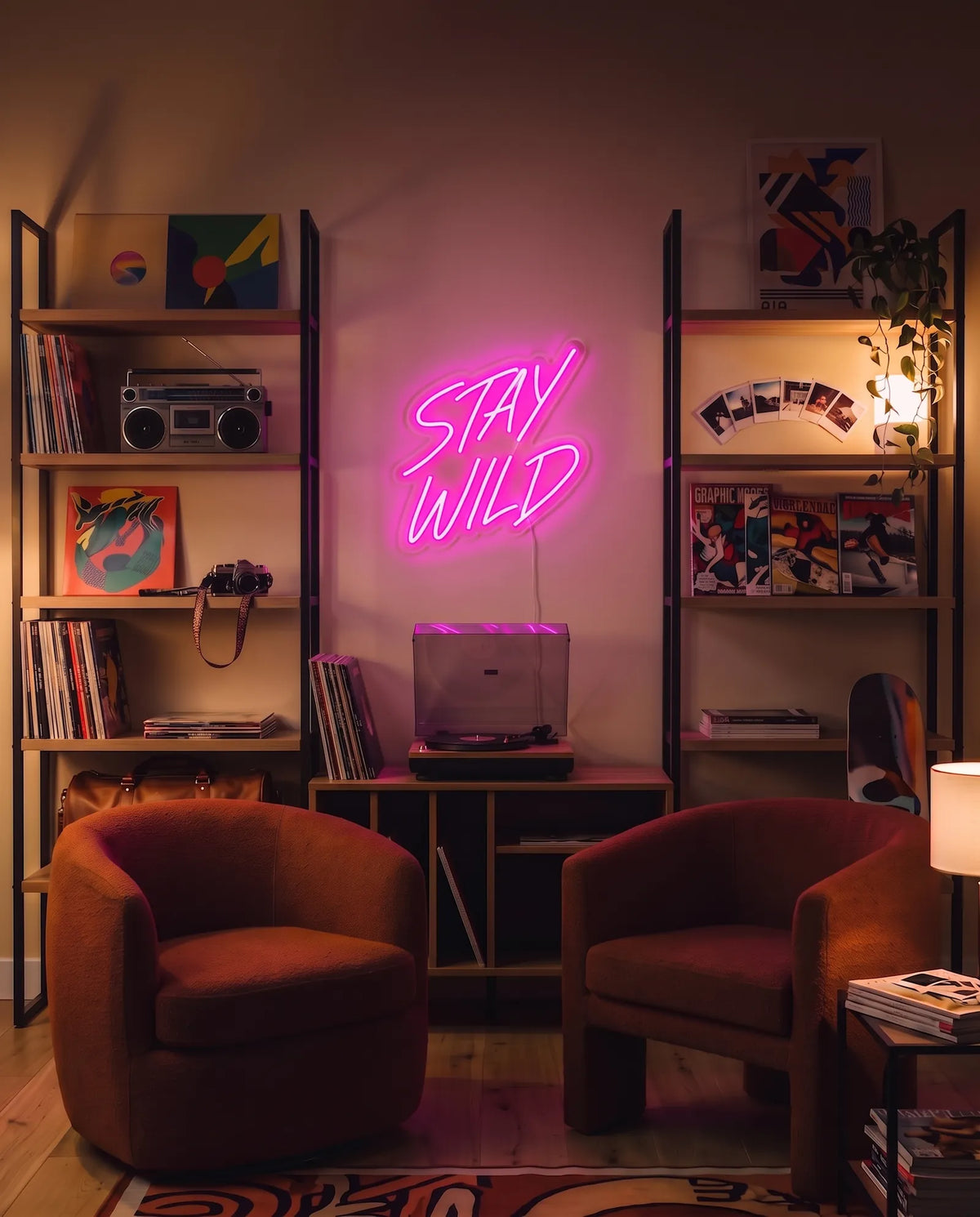 Néon Stay Wild rose allumé au-dessus d’une platine vinyle, deux fauteuils rouille, radiocassette et skate