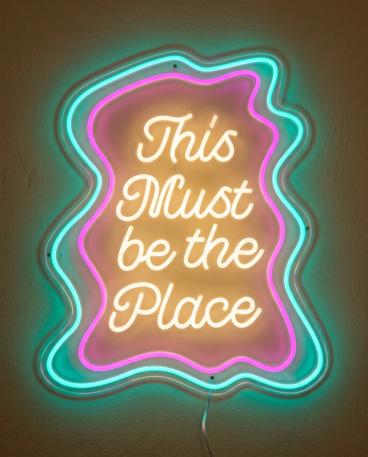 Néon This Must Be the Place de face, lettres blanc chaud dans deux contours ondulés rose et turquoise